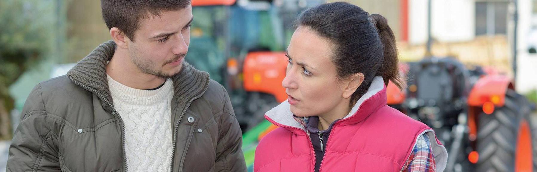 Man and woman in front of tractor, viewing information on tablet